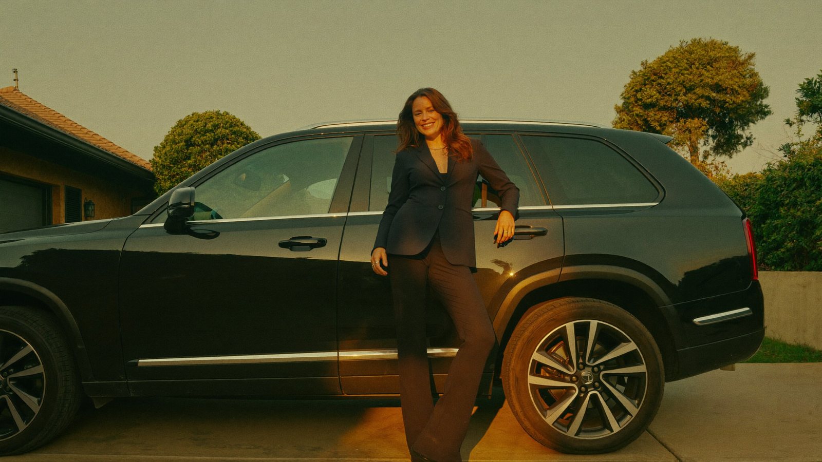 A California driver leaning against her black SUV in the driveway