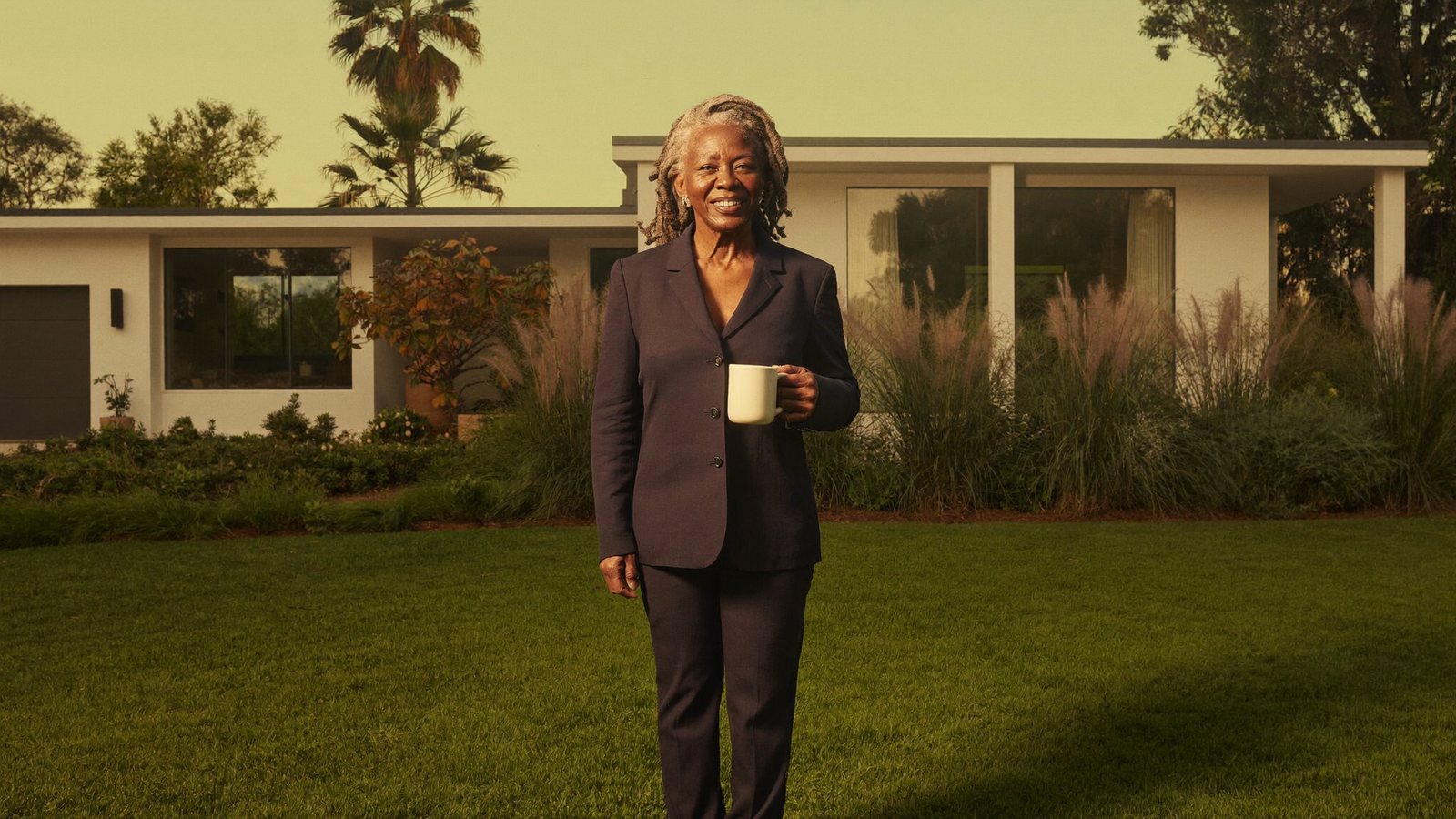 A California homeowner with a coffee mug on the lawn in front of her mid-century home