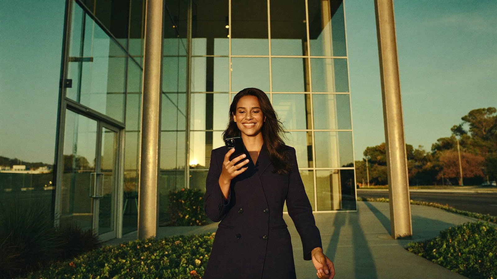 A California professional checking her phone as she walks out of an office building at golden hour